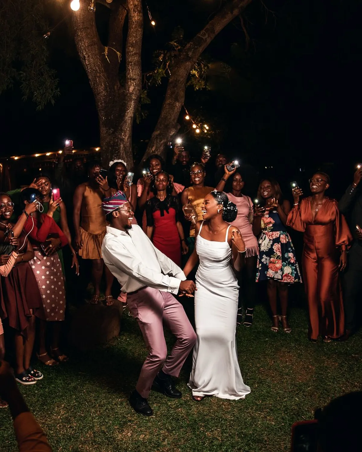 Couple dancing at night, surrounded by guests holding up phone lights